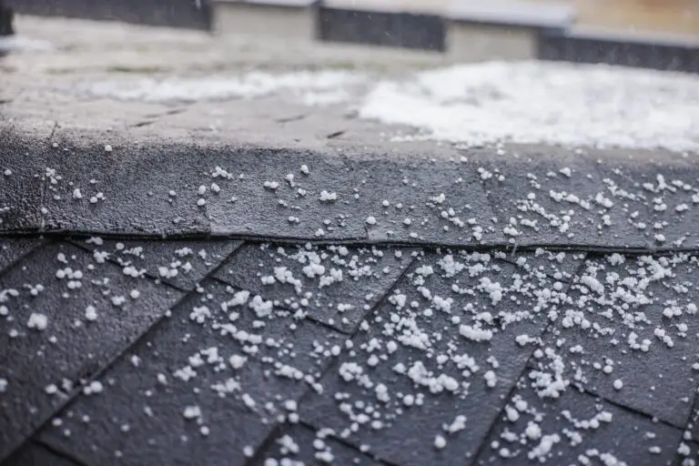 Small hailstones scattered on a dark shingled roof during a rainstorm
